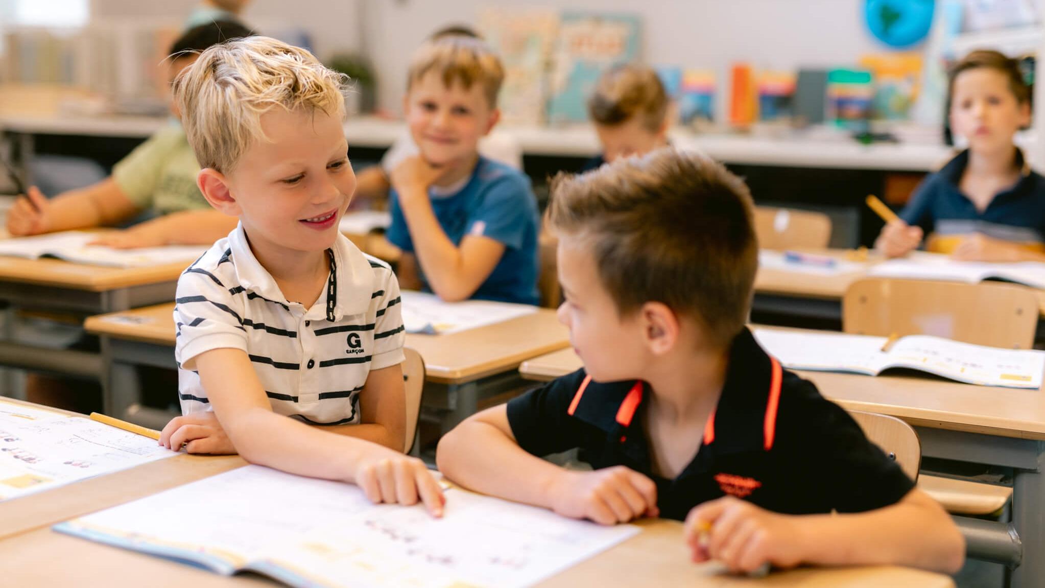 Twee leerlingen van Kindcentrum De Helmstok in Lelystad zijn met elkaar aan het praten en werken aan hun lessen. Twee leerlingen van Kindcentrum De Helmstok in Lelystad zijn met elkaar aan het praten en werken aan hun lessen.