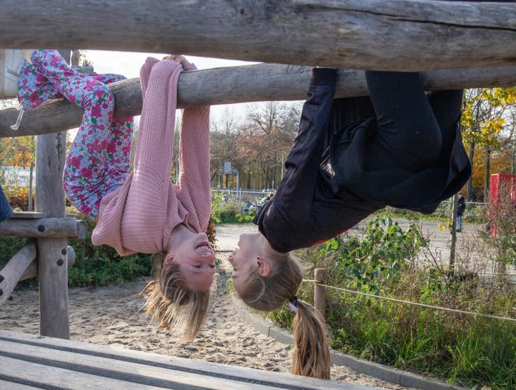 Twee meisjes hangen ondersteboven aan een speeltoestel op het schoolplein van Basisschool De Wegwijzer in Tilburg. Twee meisjes hangen ondersteboven aan een speeltoestel op het schoolplein van Basisschool De Wegwijzer in Tilburg.
