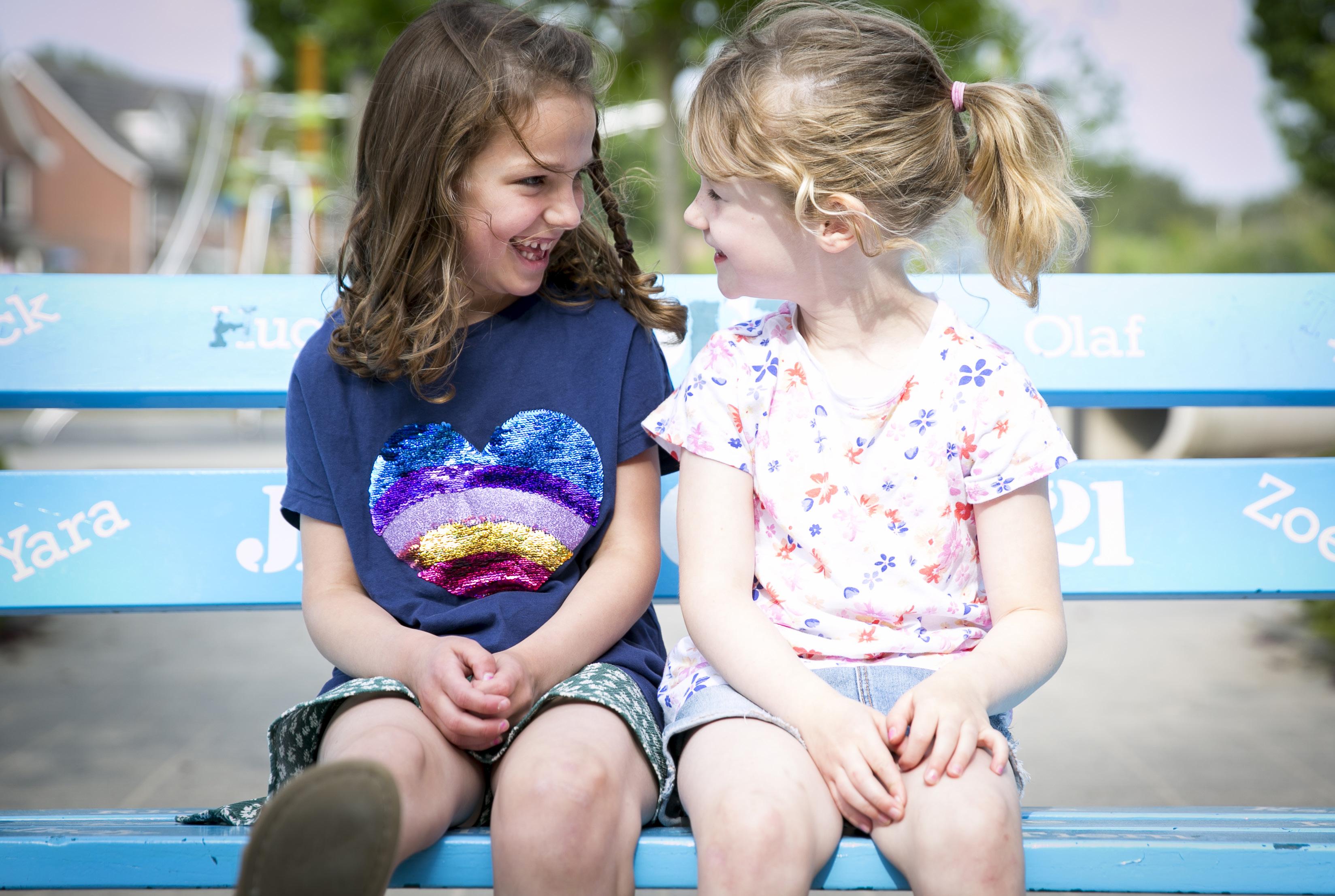 Twee meisjes lachen samen op een blauwe bank in de schoolplein van De Fontein Houten. Twee meisjes lachen samen op een blauwe bank in de schoolplein van De Fontein Houten.
