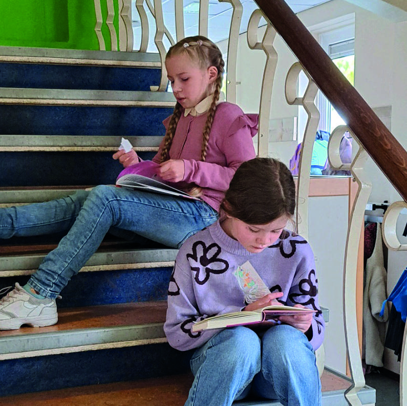 Twee meisjes lezen boeken op de trap van Christelijke Basisschool De Bron in Wezep.