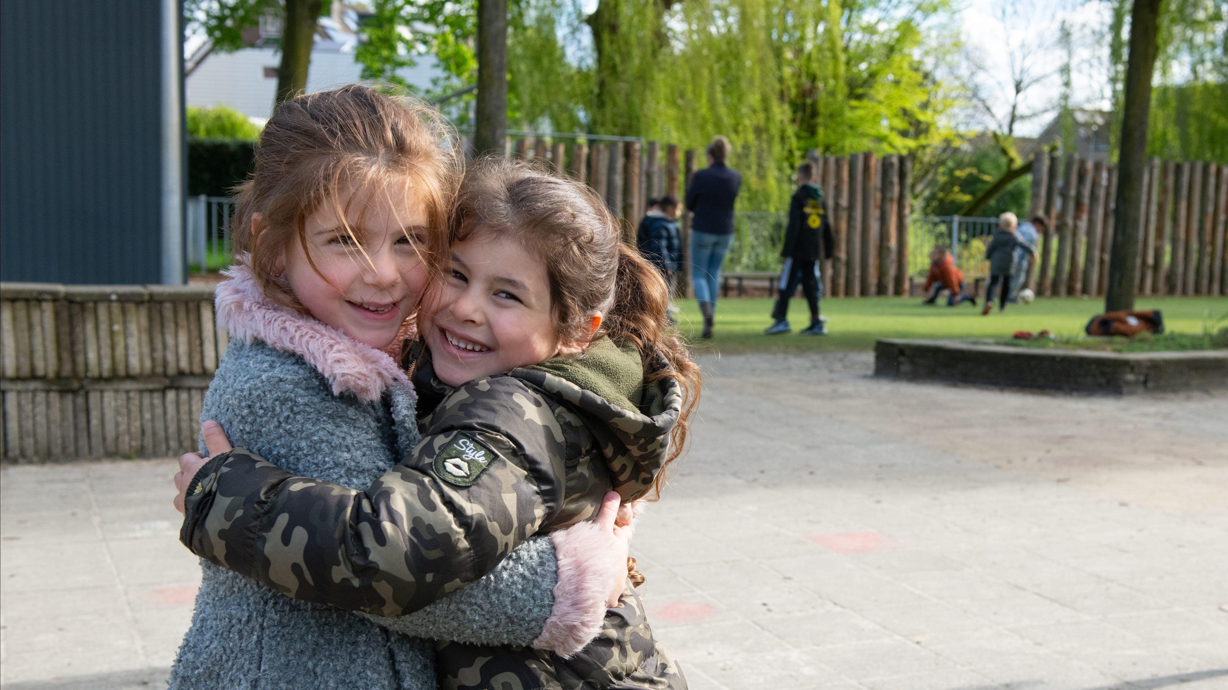 Twee meisjes omarmen elkaar vrolijk op het schoolplein van De Vliegeniers in Barneveld. Twee meisjes omarmen elkaar vrolijk op het schoolplein van De Vliegeniers in Barneveld.