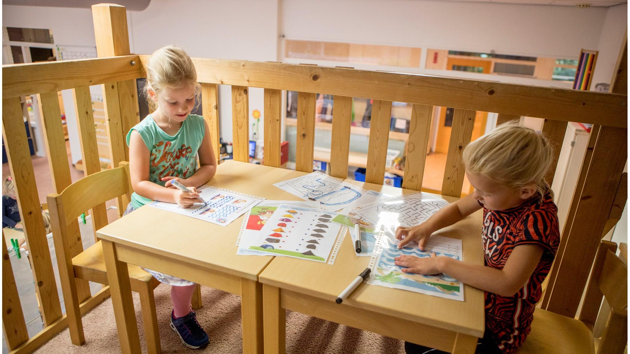 Twee meisjes van RK Basisschool De Bron in Reeuwijk zijn aan het tekenen en kleuren aan een houten tafel. Twee meisjes van RK Basisschool De Bron in Reeuwijk zijn aan het tekenen en kleuren aan een houten tafel.