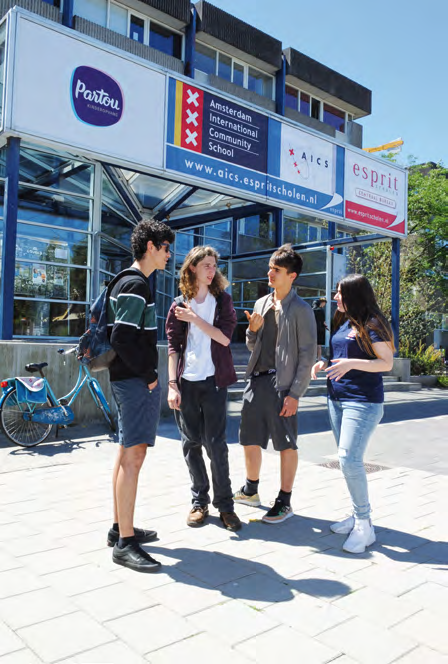 Vier studenten staan buiten de Amsterdam International Community School (AICS) en converseren met elkaar. Vier studenten staan buiten de Amsterdam International Community School (AICS) en converseren met elkaar.