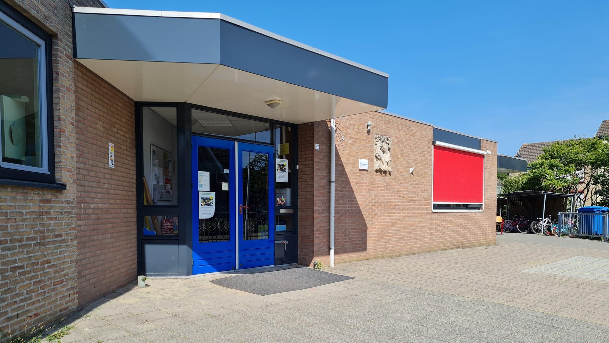 Voorkant van Basisschool De Driesprong in Hoek met blauwe deuren en een helderblauwe lucht. Voorkant van Basisschool De Driesprong in Hoek met blauwe deuren en een helderblauwe lucht.